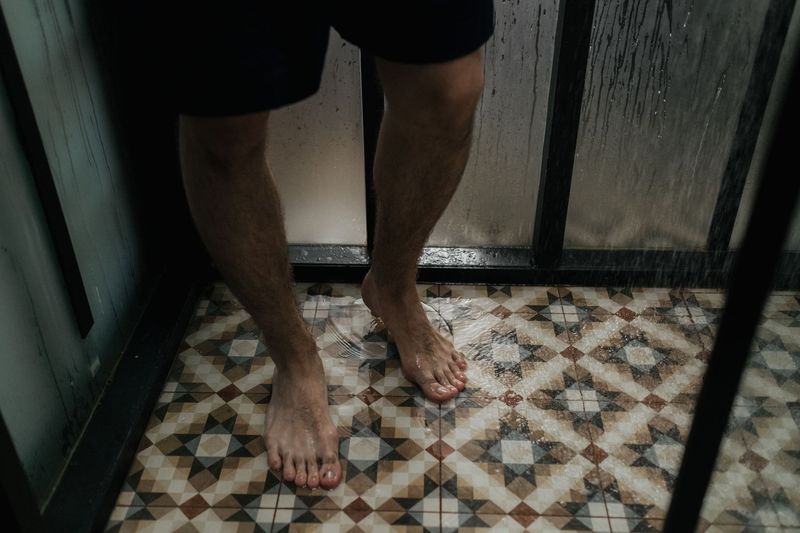 Bare føtter på et fliselagt dusjgulv med vann og duggete glassvegger