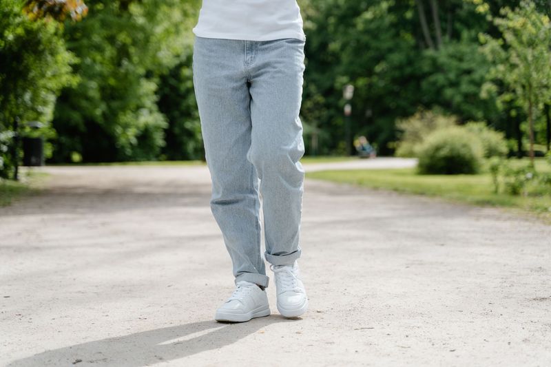 Person i olabukse og hvite joggesko går på en gruset sti i en grønn park