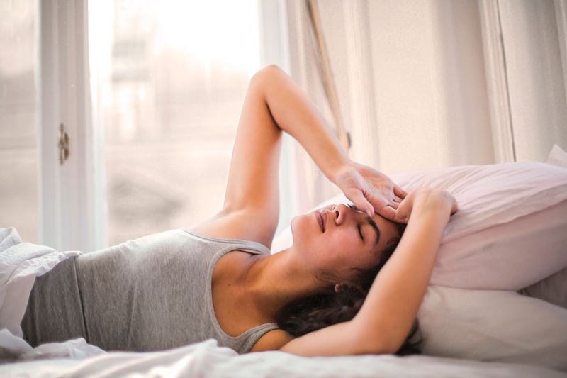 Kvinne hviler i sengen mens mykt morgenlys strømmer inn gjennom vinduet