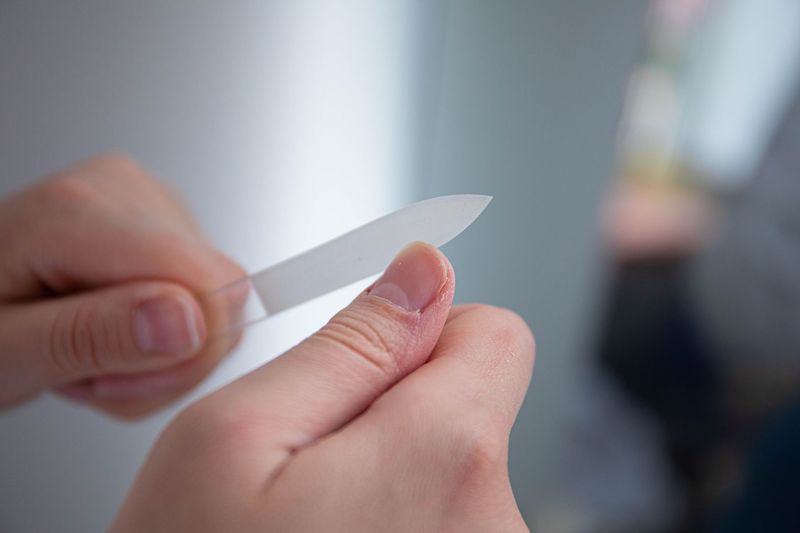 Nærbilde av en hånd som filer en negl med en glassfil