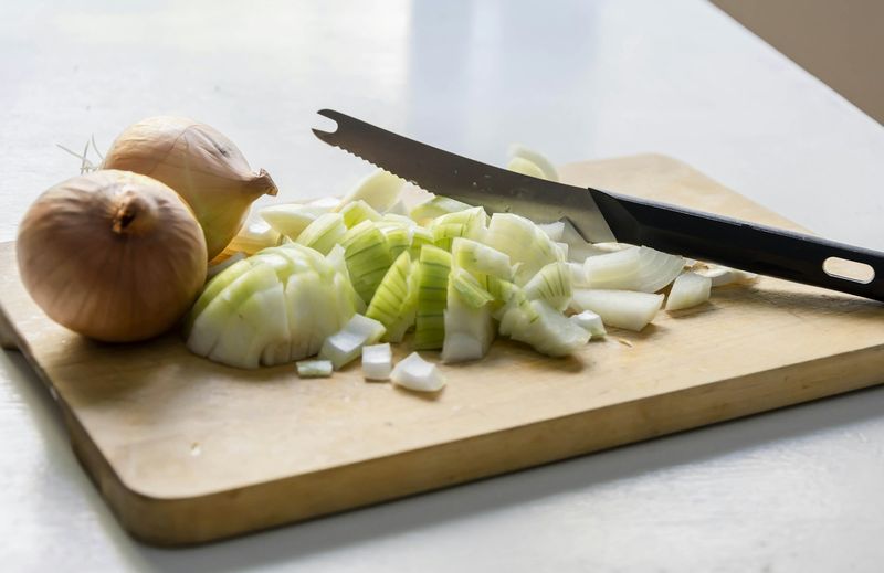 Hakket løk og hele løk på et trebrett ved siden av en kniv