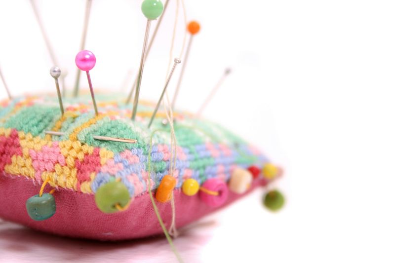 Fargerike knappenåler og perler stukket inn i en nålepute