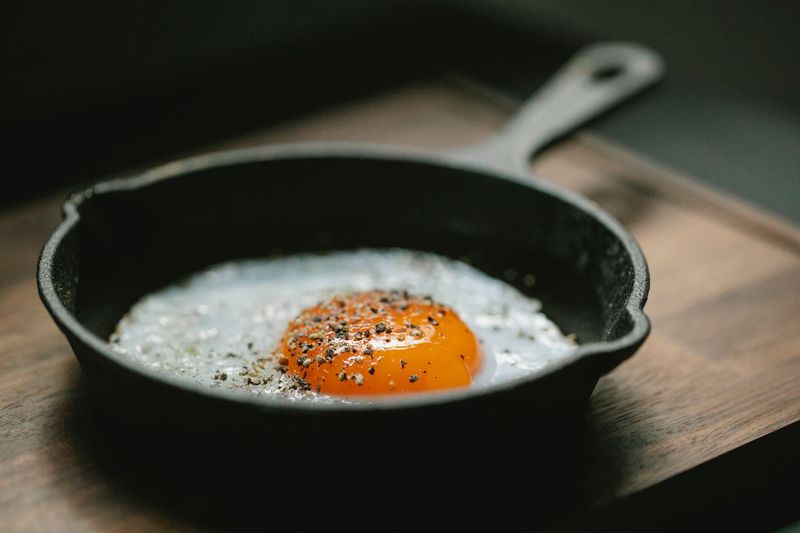 Stekt egg med pepper i en liten støpejernspanne på en trefjøl