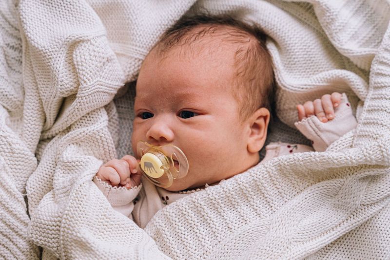 Baby med narresmokk pakket inn i et mykt beige strikketeppe